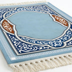 Light blue prayer mat close-up with navy and brown ornate arch, white fringed edge