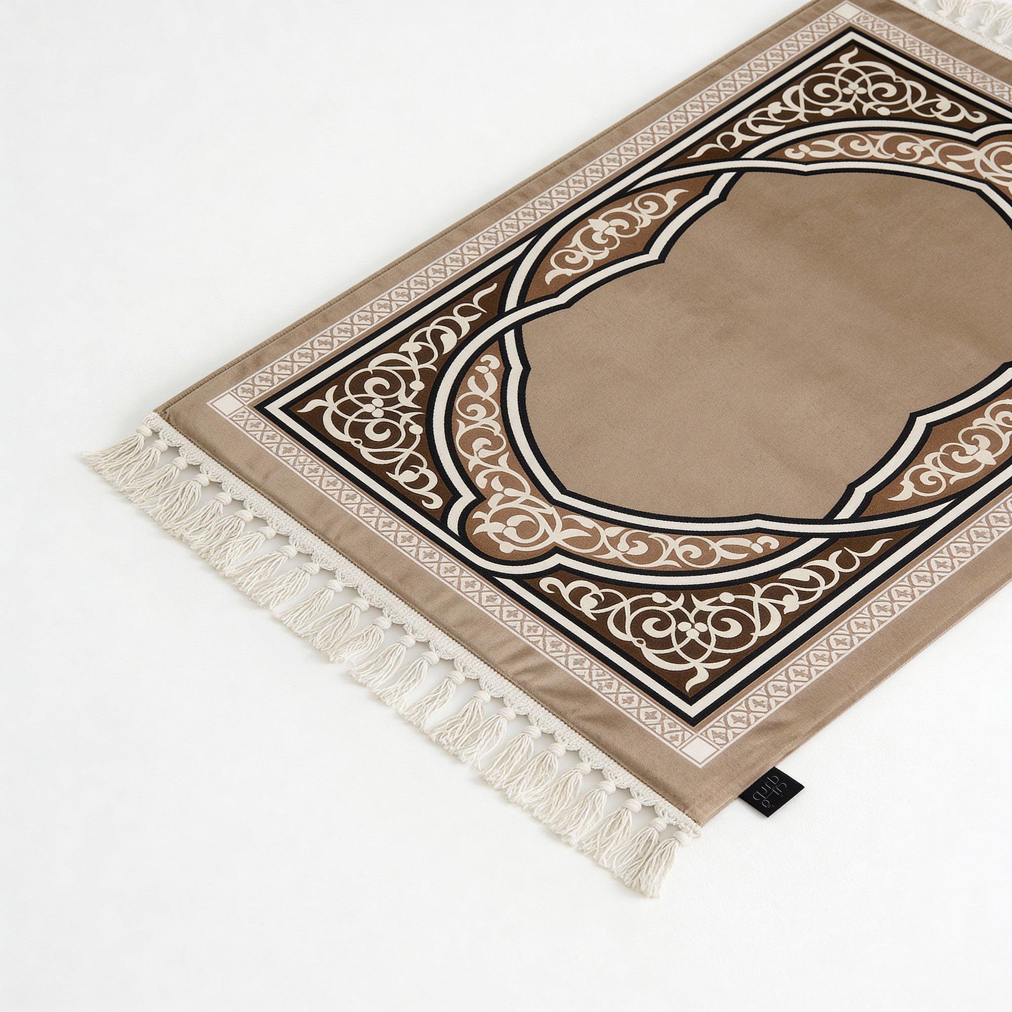 Beige prayer mat with brown arch design and white tassels, black tag at corner