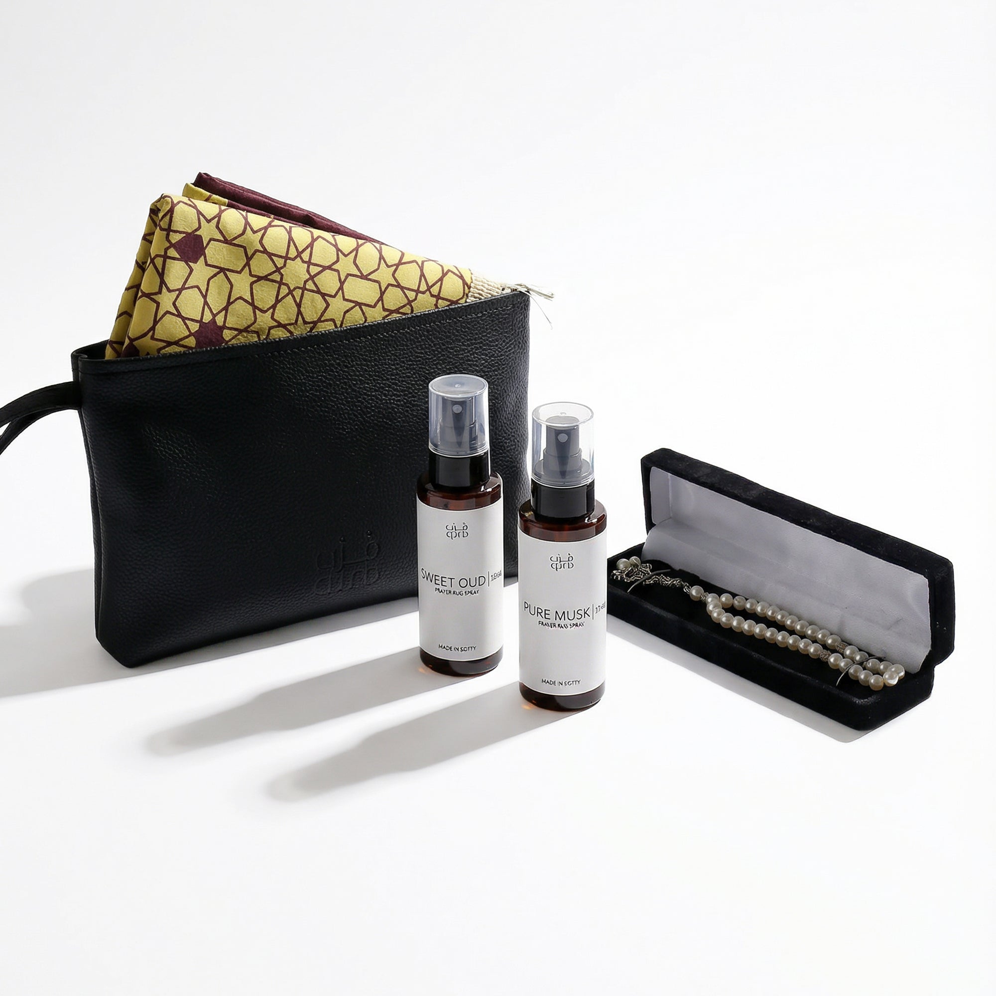 Open gift set with black case, folded patterned fabric, white prayer beads, and two spray bottles